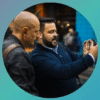 Two men engaged in discussion while reviewing photos on a camera outdoors.